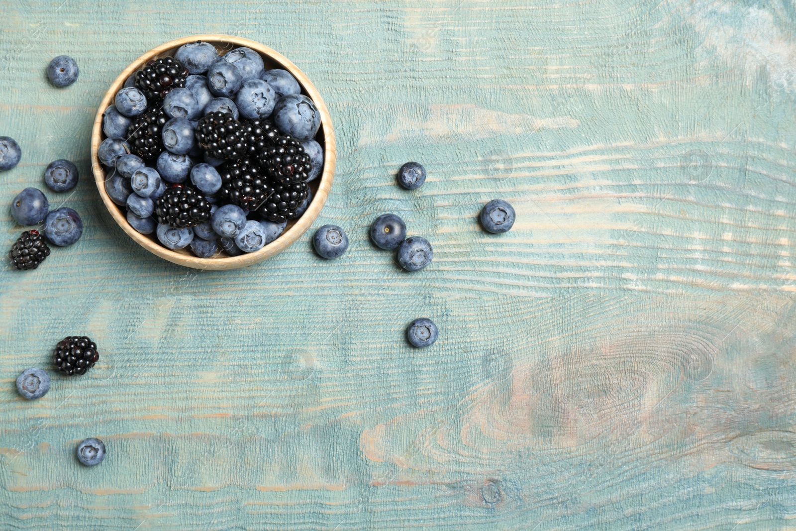 Photo of Blueberries and blackberries on blue wooden table, flat lay. Space for text