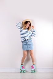 Young woman with retro roller skates near white wall