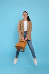 Beautiful young woman with stylish leather backpack jumping on turquoise background