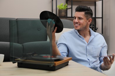 Happy man choosing vinyl record to play with turntable at home