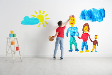 Image of Little boy drawing on white wall indoors, back view