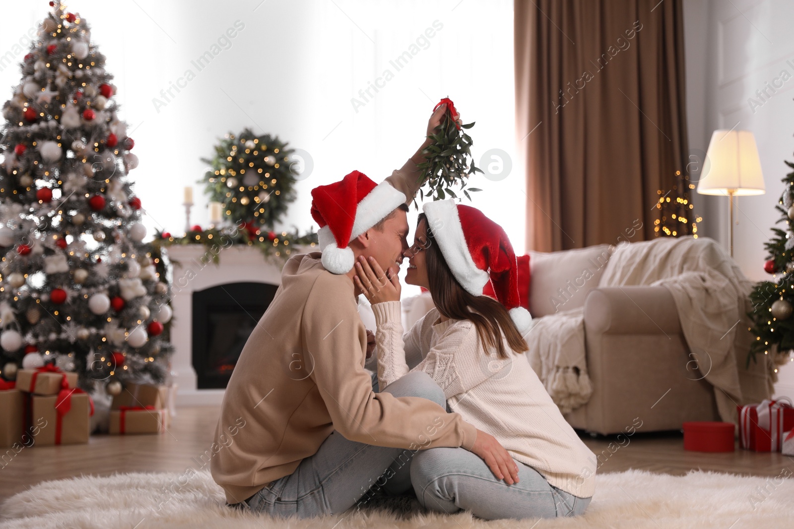 Photo of Couple kissing under mistletoe in room decorated for Christmas