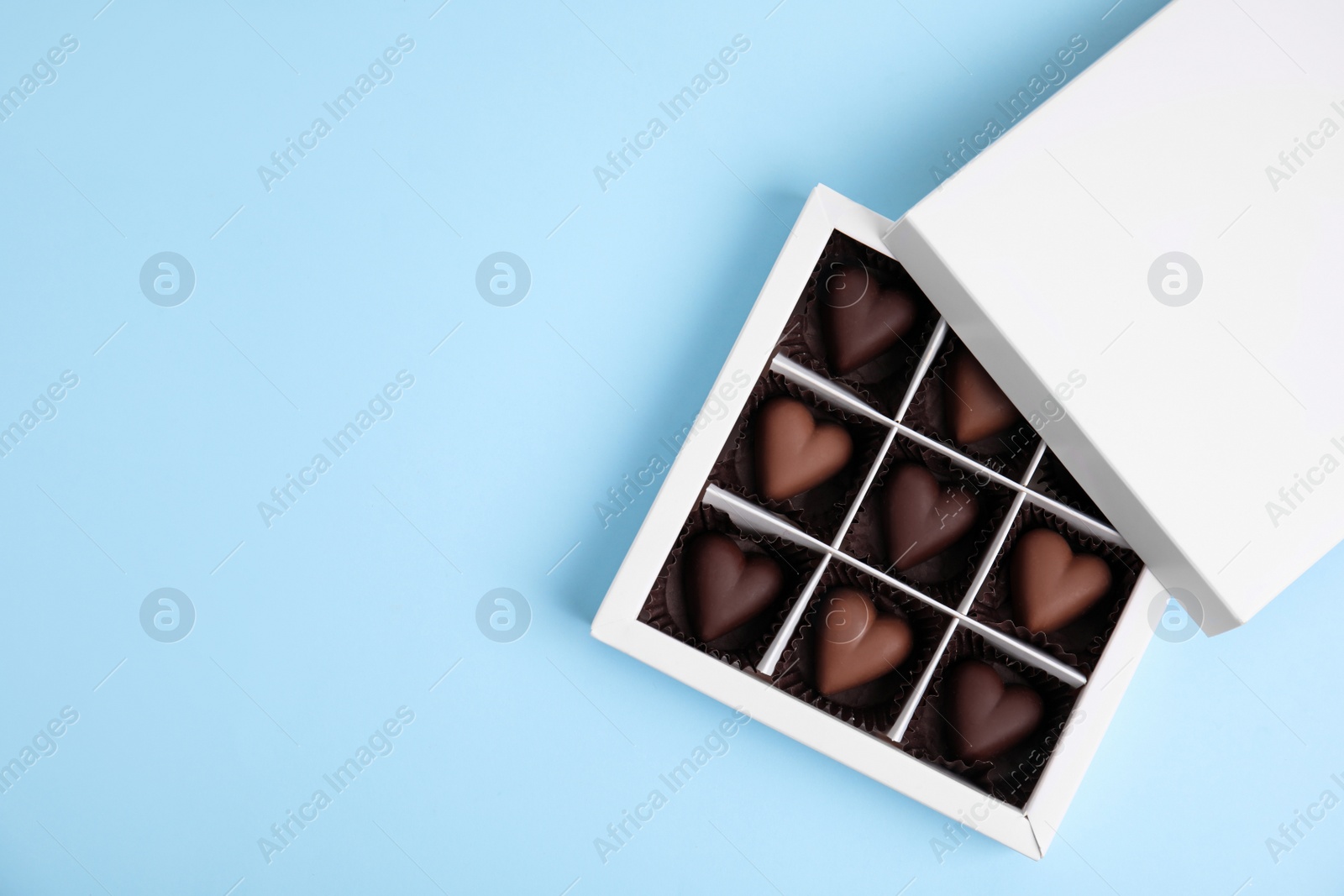 Photo of Tasty heart shaped chocolate candies on light blue background, flat lay with space for text. Happy Valentine's day