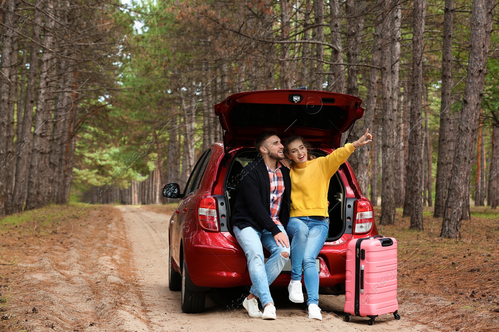 Photo of Young couple sitting in car trunk and suitcase on forest road