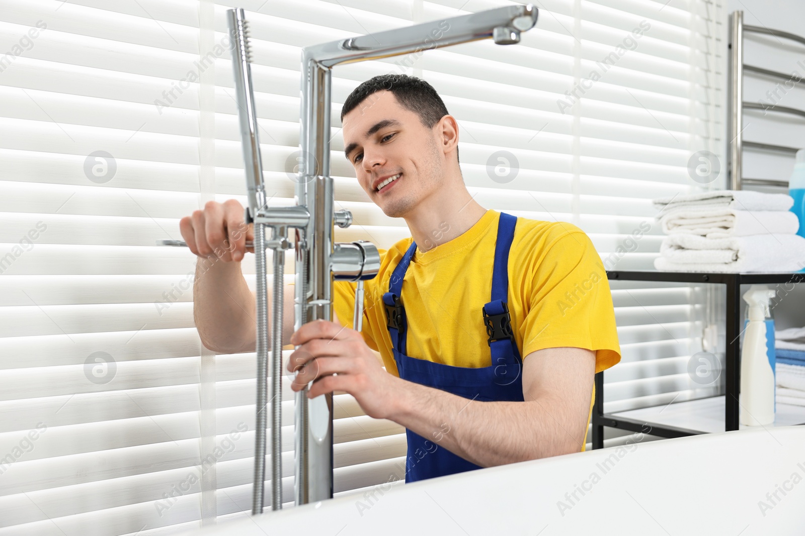 Photo of Smiling plumber repairing faucet with spanner in bathroom