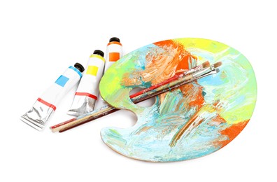 Photo of Dirty artist's palette with brushes and tubes of paint on white background