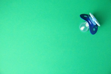 Photo of Blue baby pacifier on green background, top view. Space for text