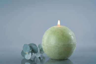 Photo of Burning green candle and eucalyptus branch on light grey background