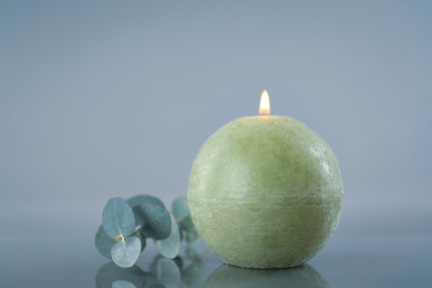 Burning green candle and eucalyptus branch on light grey background