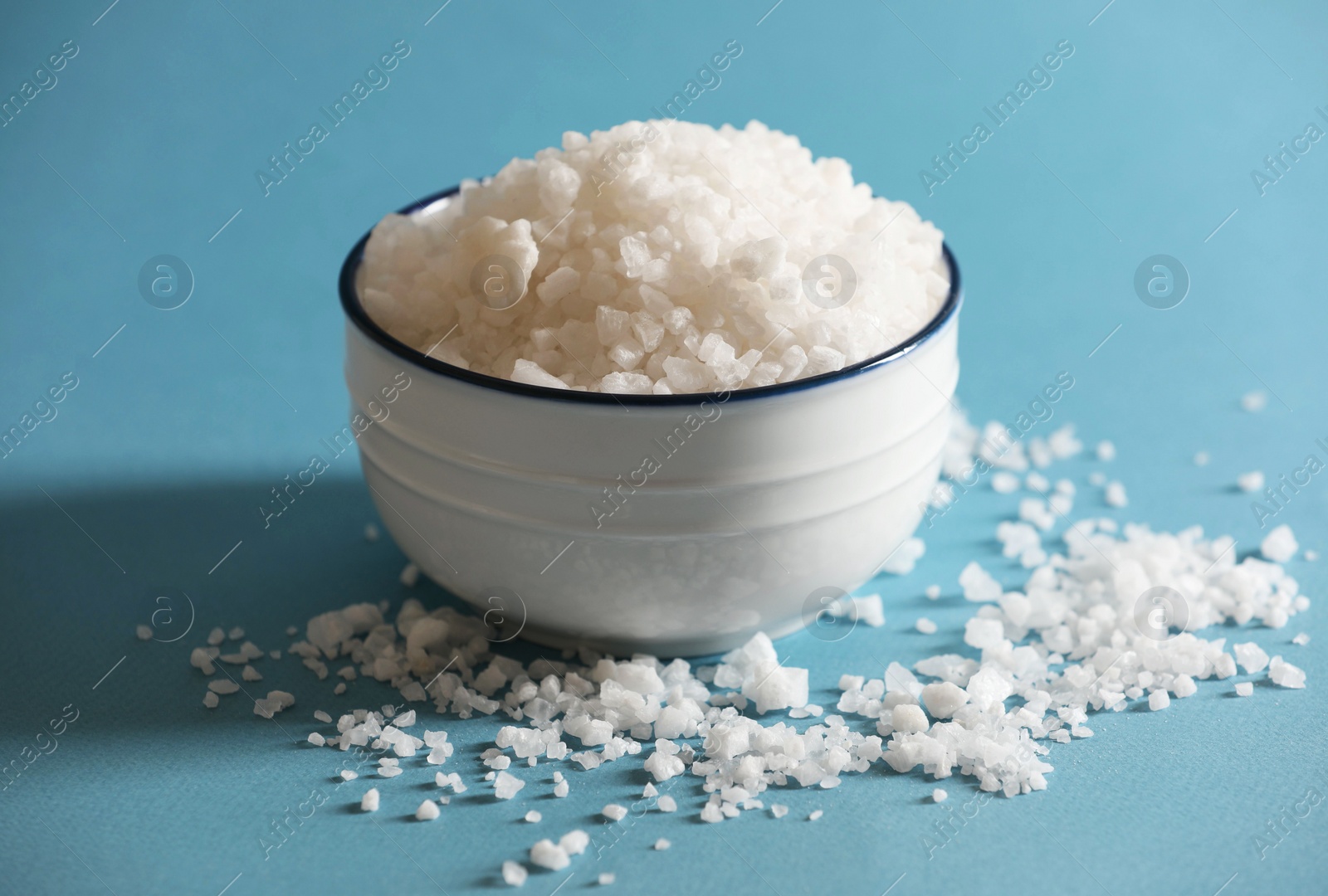 Photo of Organic salt in bowl on light blue background, closeup