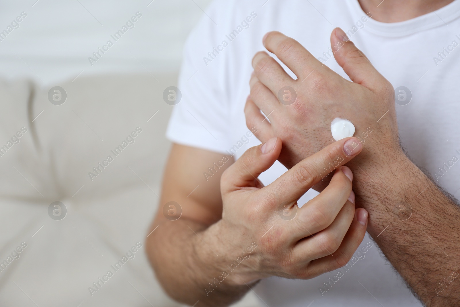 Photo of Man applying cream onto hand on sofa, closeup