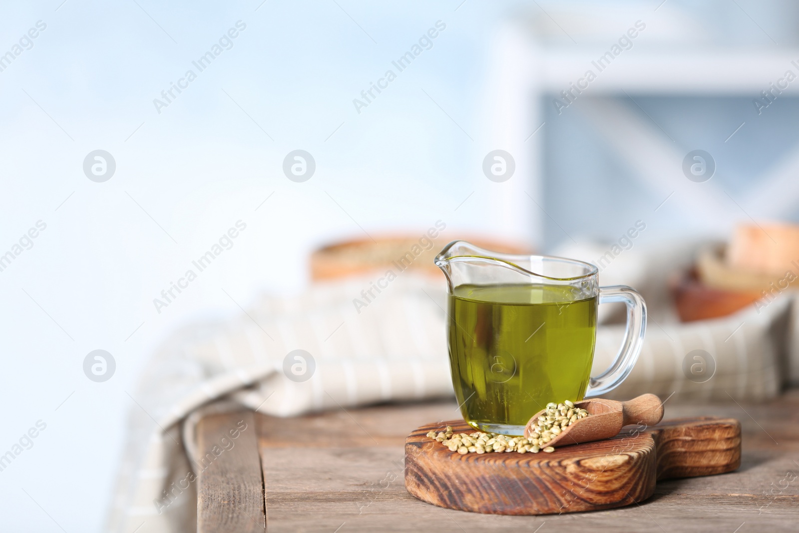 Photo of Jug with hemp oil and seeds on wooden table. Space for text