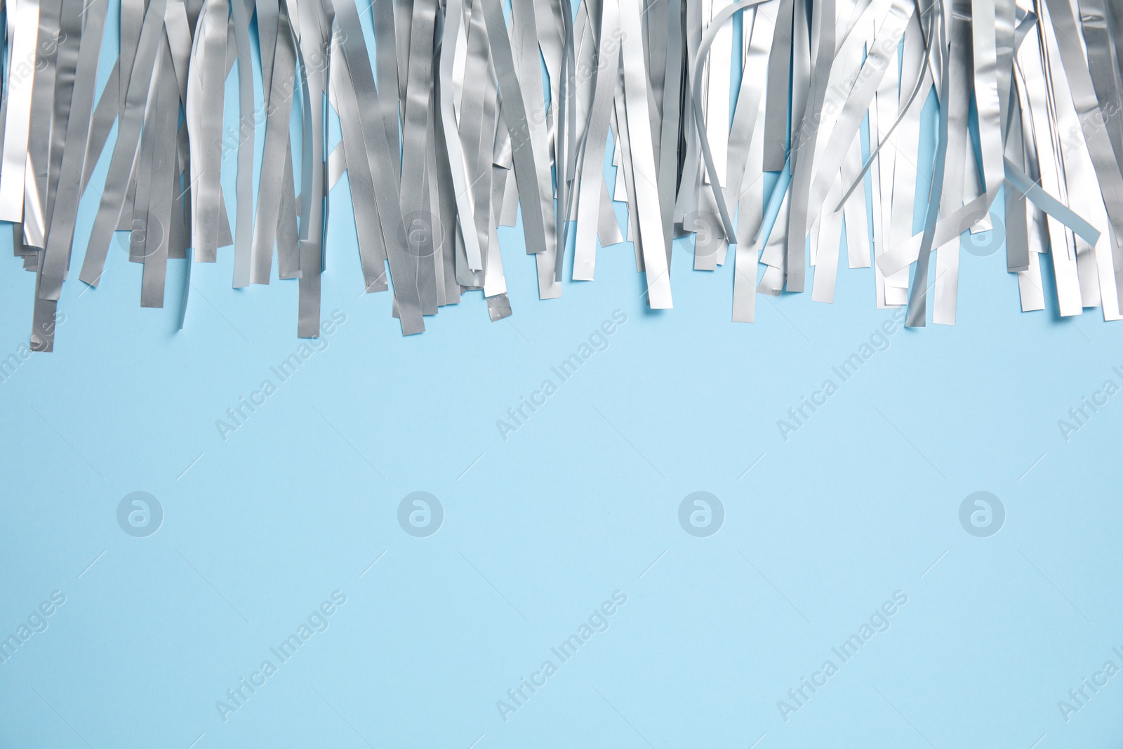 Photo of Silver tinsel on light blue background, top view. Space for text
