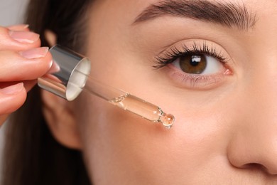 Young woman applying essential oil onto face, closeup