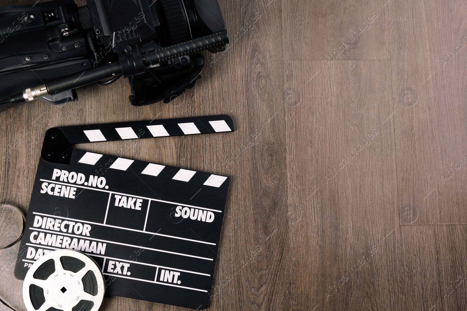 Photo of Modern video camera, movie clapper and reel on wooden table, flat lay. Space for text