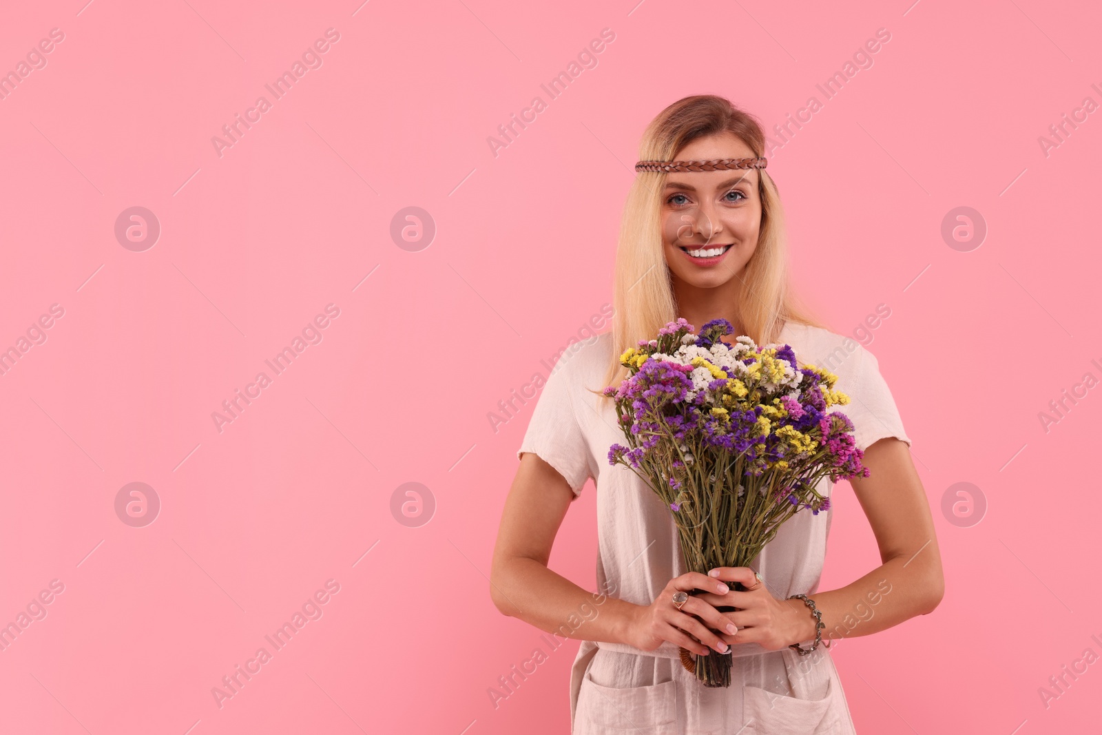 Photo of Portrait of smiling hippie woman with bouquet of flowers on pink background. Space for text