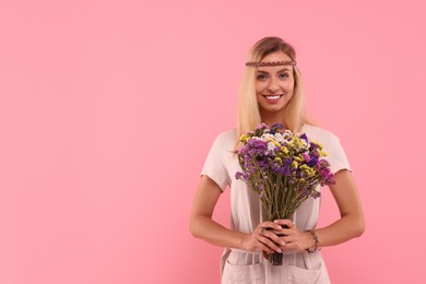 Portrait of smiling hippie woman with bouquet of flowers on pink background. Space for text