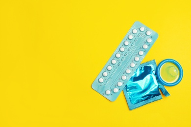 Photo of Condoms and birth control pills on yellow background, flat lay with space for text. Safe sex concept