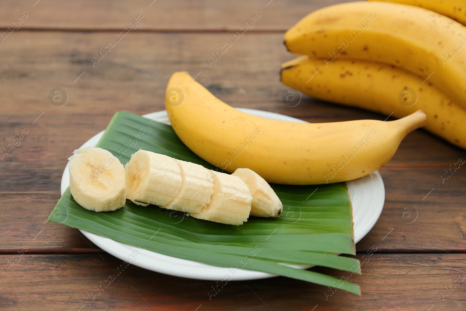 Photo of Delicious ripe bananas and fresh leaf on wooden table