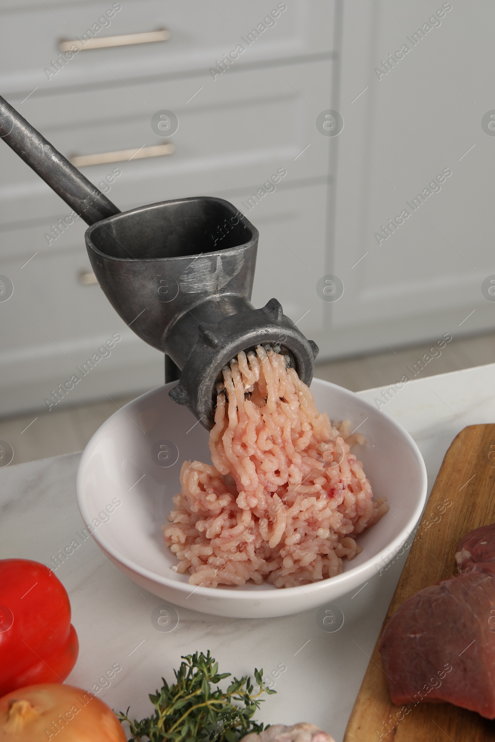 Photo of Metal meat grinder with chicken mince and products on white marble table in kitchen