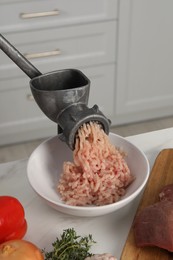 Metal meat grinder with chicken mince and products on white marble table in kitchen