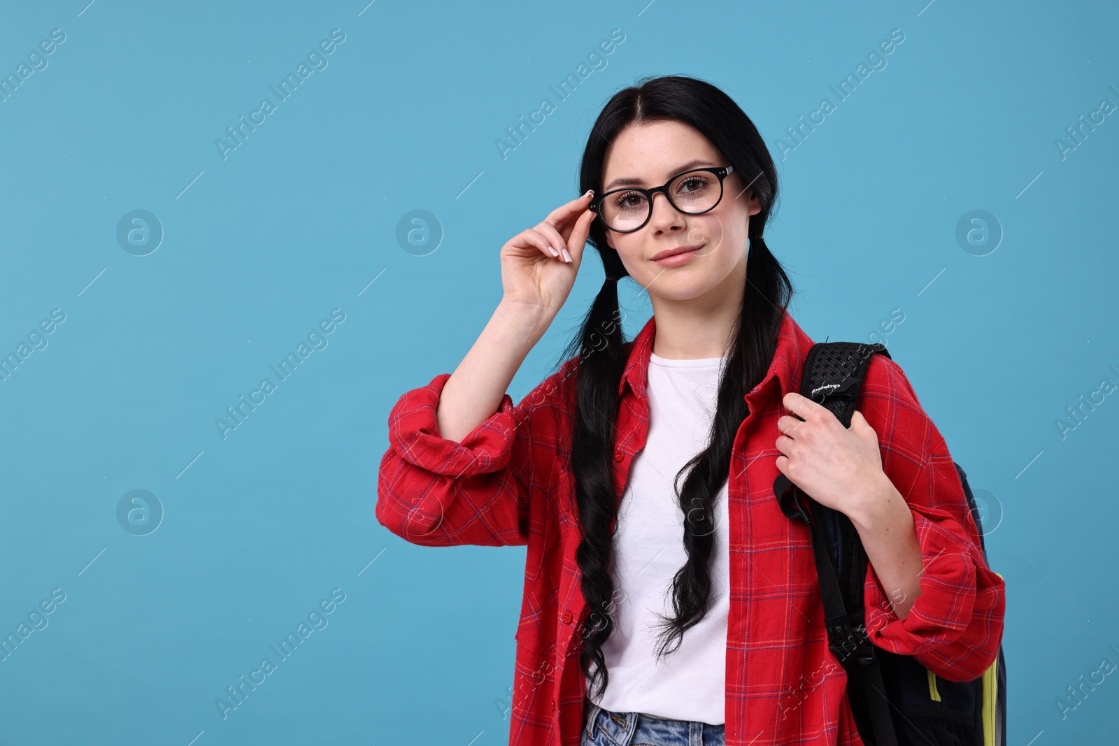Photo of Student in glasses with backpack on light blue background. Space for text