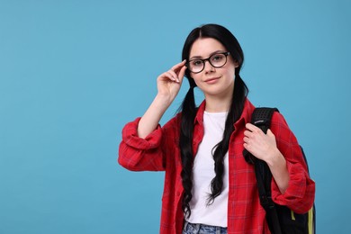 Photo of Student in glasses with backpack on light blue background. Space for text