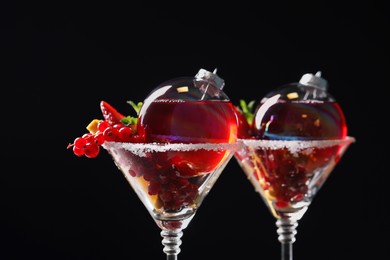 Photo of Creative presentation of Christmas Sangria cocktail in baubles and glasses on black background, closeup