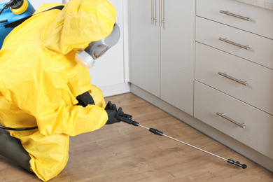 Pest control worker in protective suit spraying pesticide indoors