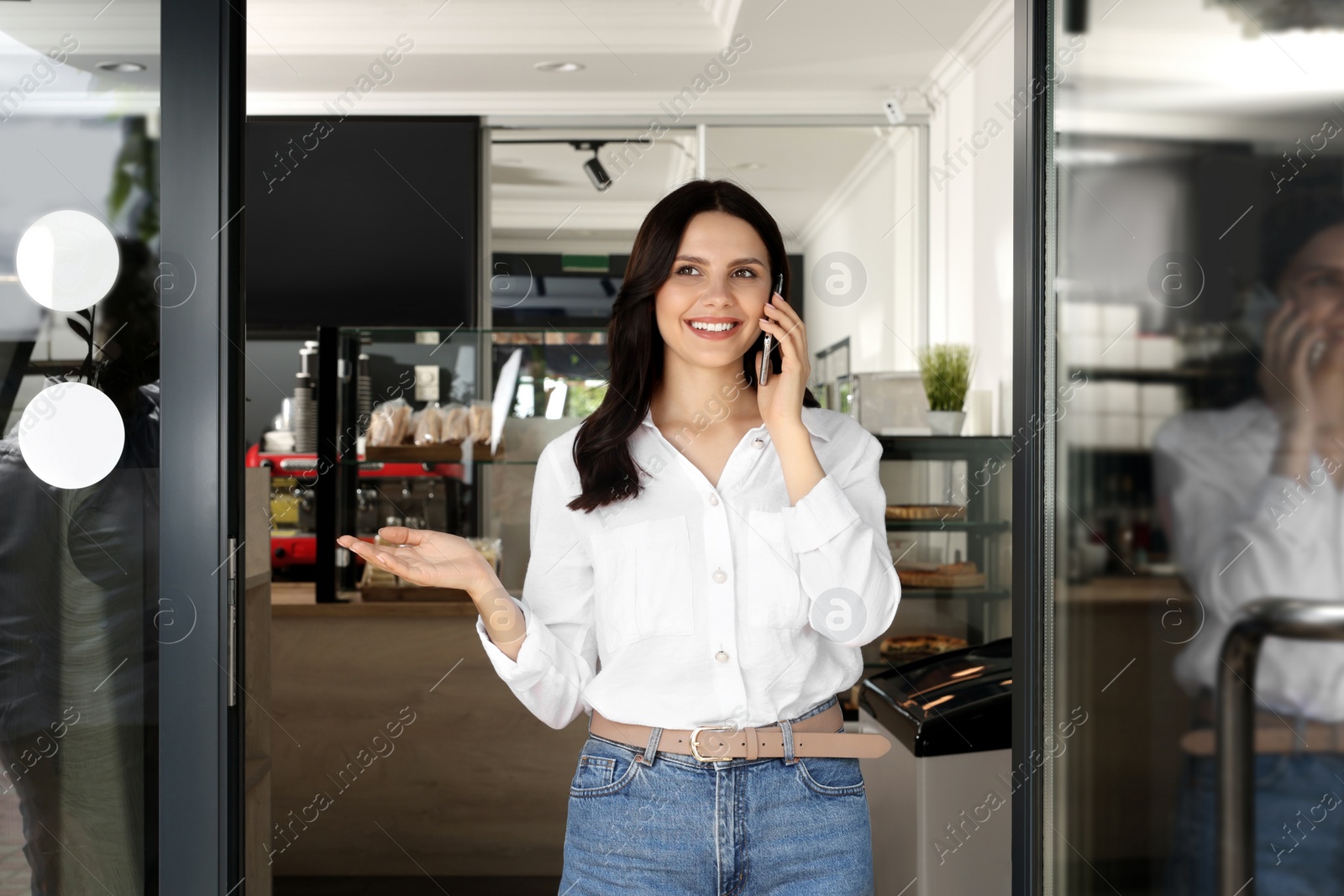 Photo of Business owner talking on smartphone at door of her cafe