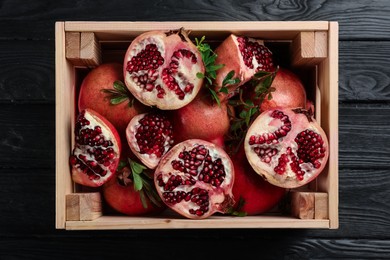 Delicious ripe pomegranates on black wooden table, top view