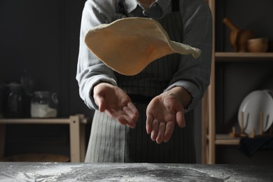 Woman tossing pizza dough at table in kitchen, closeup