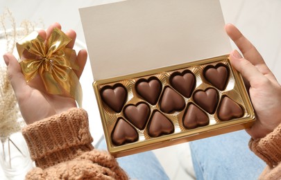 Photo of Woman with box of heart shaped chocolate candies indoors, closeup