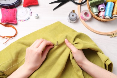 Woman with sewing needle and thread embroidering on cloth at white wooden table, top view