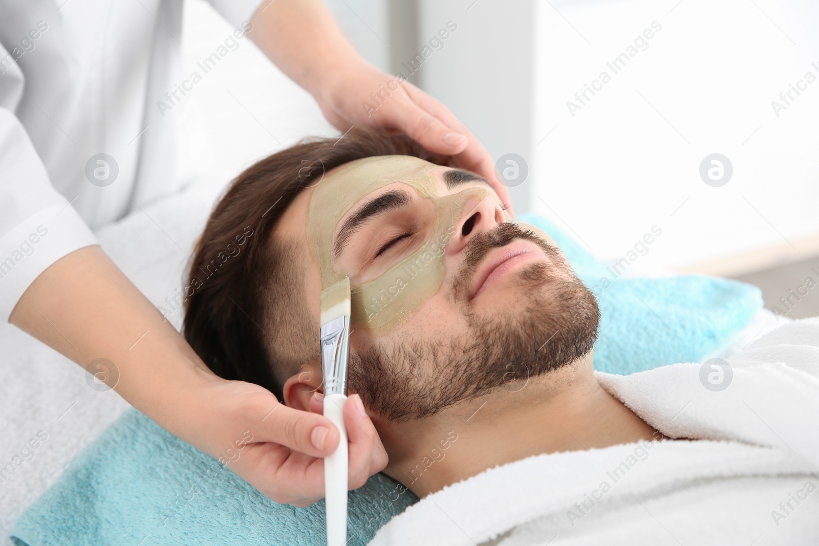 Photo of Cosmetologist applying mask on client's face in spa salon