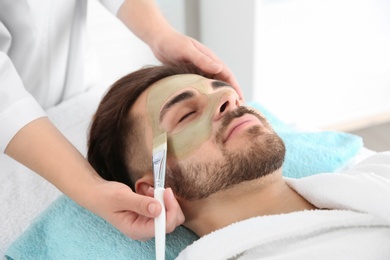 Photo of Cosmetologist applying mask on client's face in spa salon