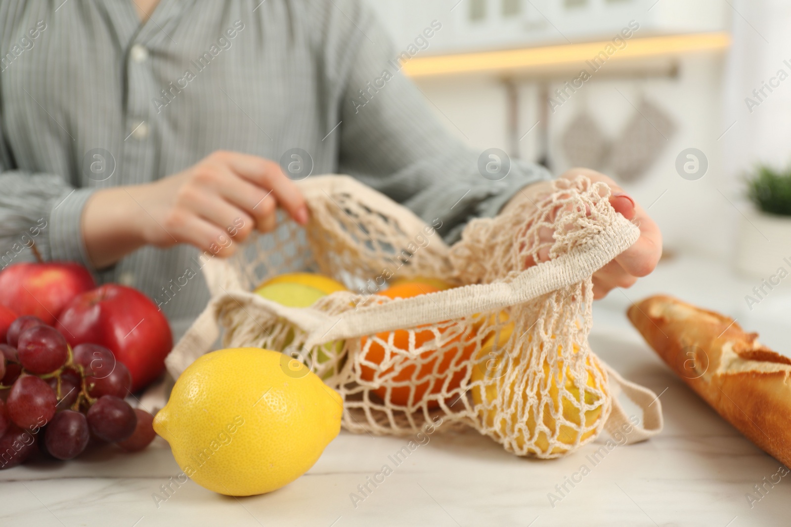 Photo of Woman with string bag of fresh fruits at light marble table, closeup