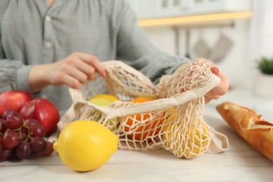 Photo of Woman with string bag of fresh fruits at light marble table, closeup