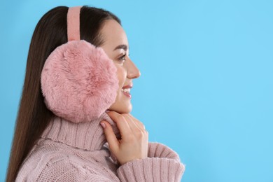 Beautiful young woman wearing earmuffs on light blue background. Space for text