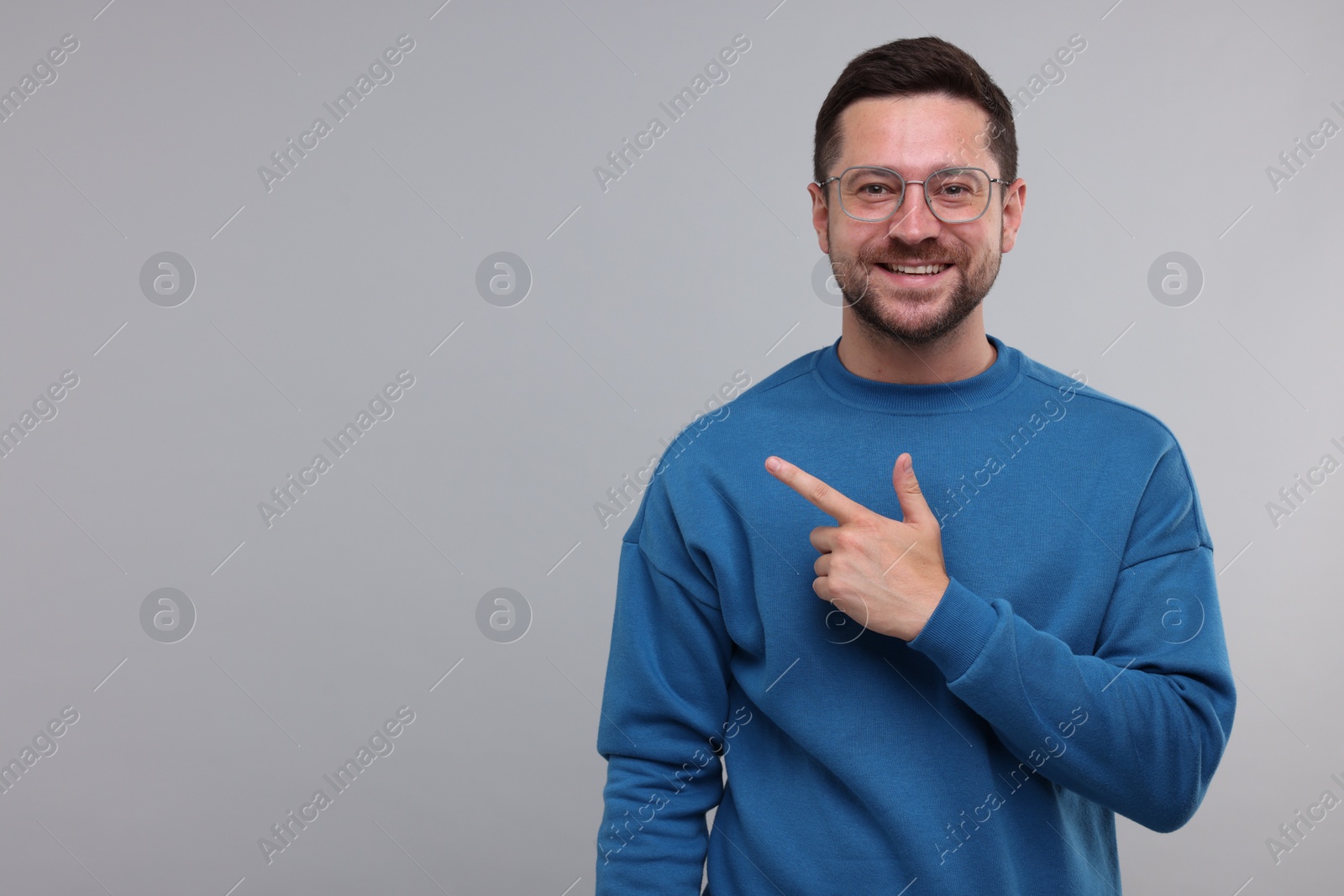 Photo of Special promotion. Smiling man pointing at something on light grey background. Space for text