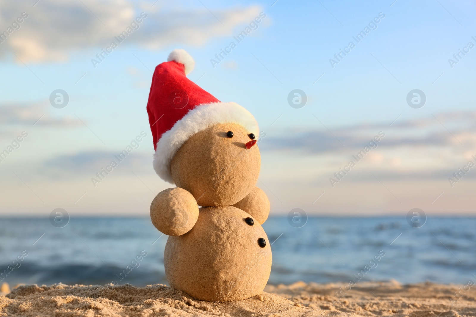 Photo of Snowman made of sand with Santa hat on beach near sea. Christmas vacation