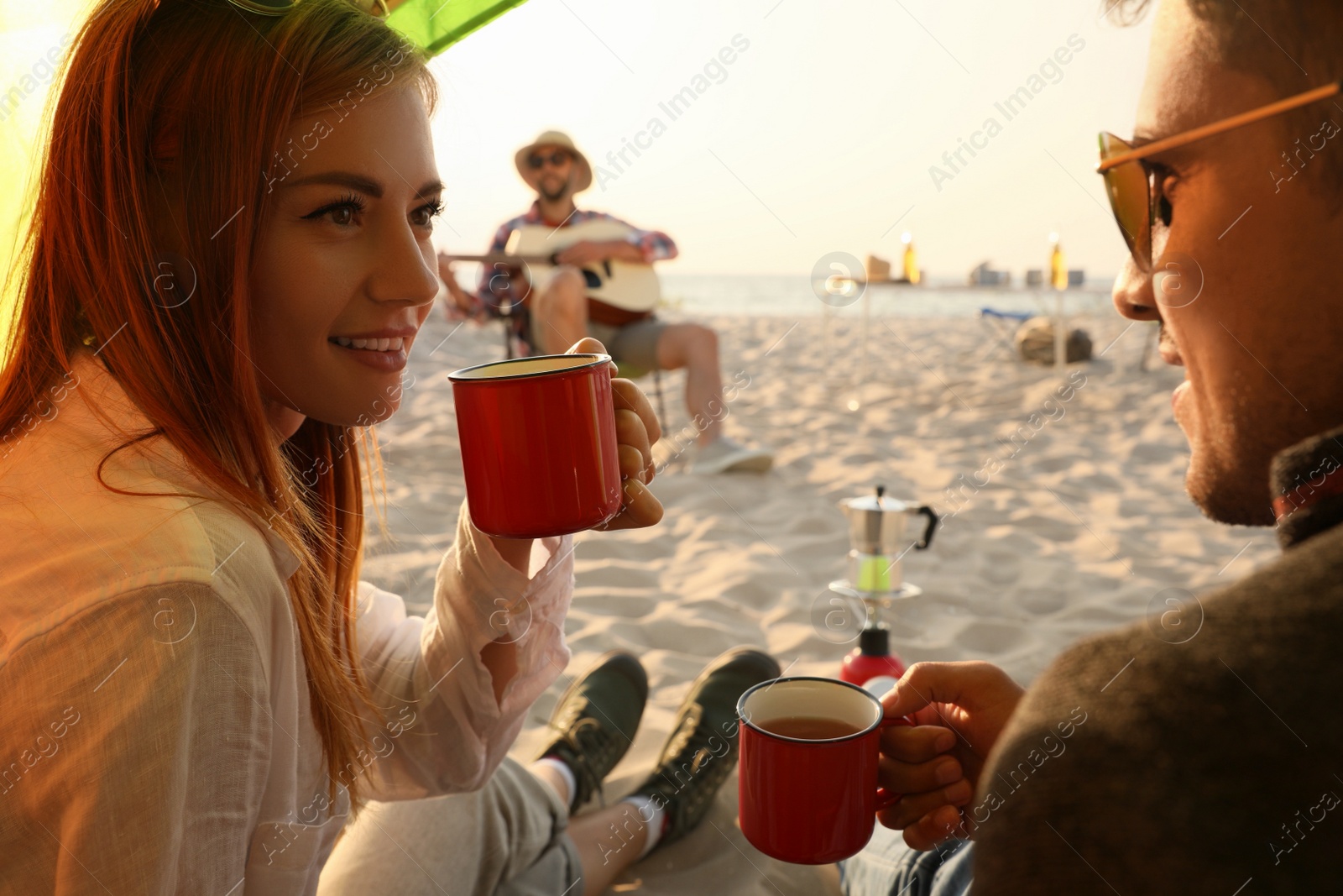 Photo of Friends resting on sandy beach. View from camping tent