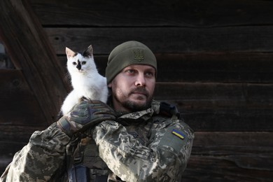 Ukrainian soldier rescuing animal. Little stray cat on man's shoulder, closeup. Space for text