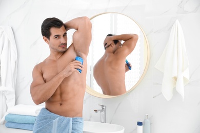 Handsome young man applying deodorant in bathroom