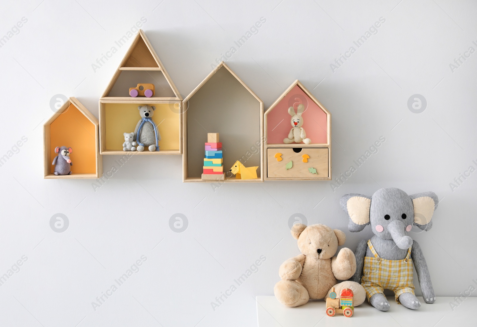 Photo of House shaped shelves and table with toys in children's room. Interior design