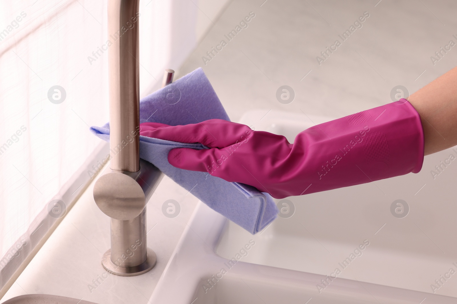 Photo of Woman in gloves cleaning faucet of kitchen sink with rag, closeup