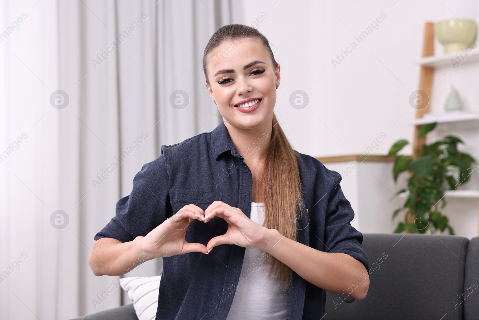 Photo of Happy woman showing heart gesture with hands at home