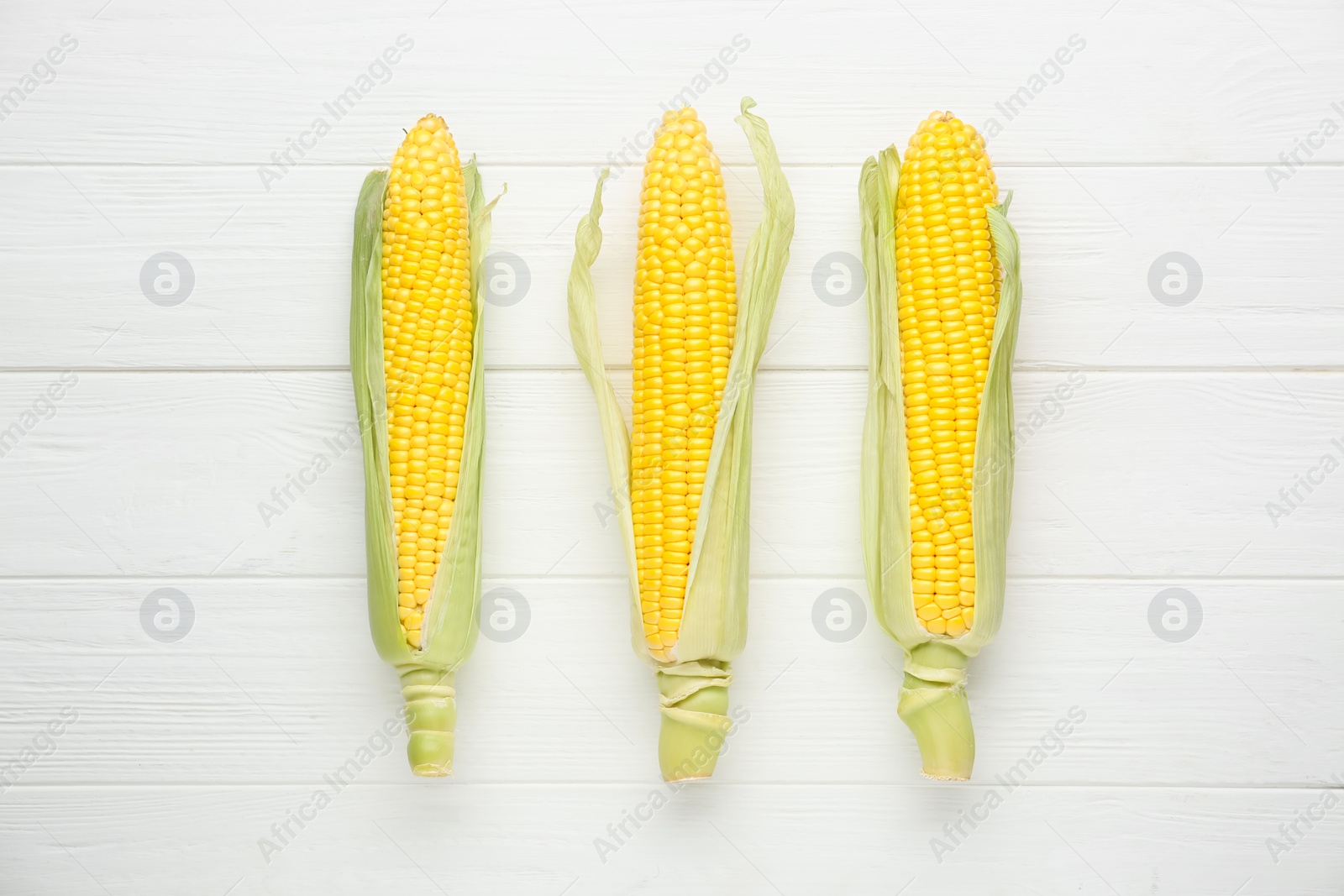 Photo of Tasty fresh corn cobs on white wooden table, flat lay