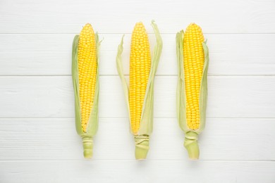 Photo of Tasty fresh corn cobs on white wooden table, flat lay