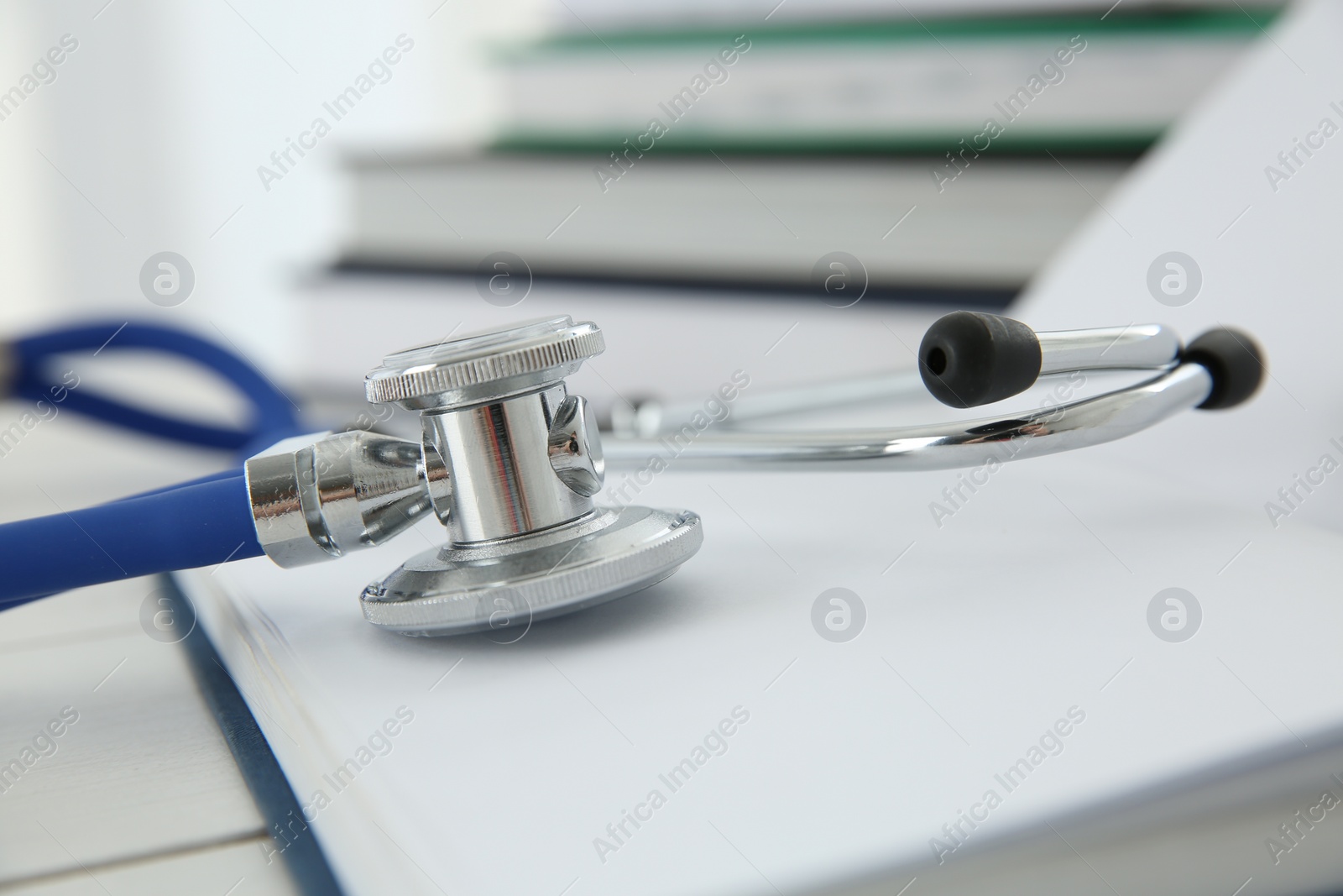 Photo of One new medical stethoscope and books on white wooden table, closeup